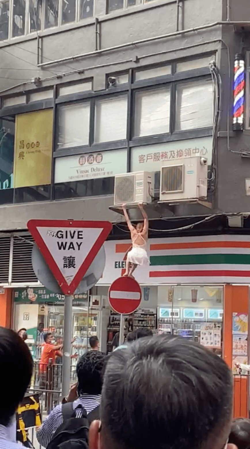 女子再慢慢爬落馬路上的標示牌頂。